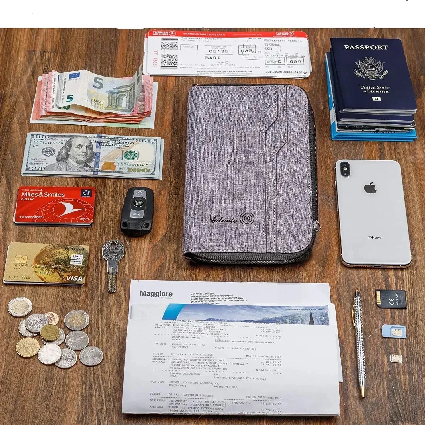 Portafoglio da viaggio grigio su tavolo di legno con passaporto, smartphone, biglietti aerei, contanti, carte di credito, chiavi e monete.