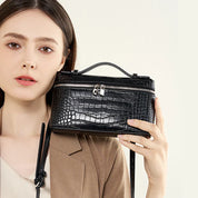 Donna con borsa a tracolla in pelle nera effetto coccodrillo, chiusura con zip e manico superiore. Elegante accessorio moda femminile.