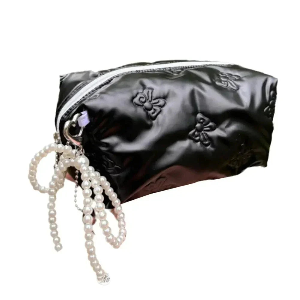 Astuccio cosmetico nero in raso con cerniera, decorato con motivi floreali e perline bianche. Elegante e pratico per trucchi e accessori.