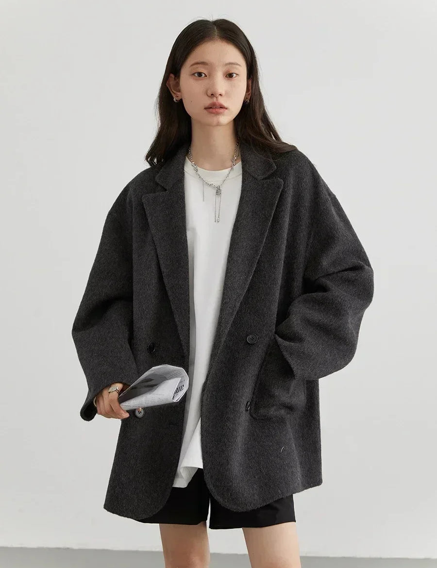 Donna con giacca oversize grigia, maglietta bianca e pantaloncini neri. Moda casual autunnale, stile minimalista. Accessori: collana e borsa.