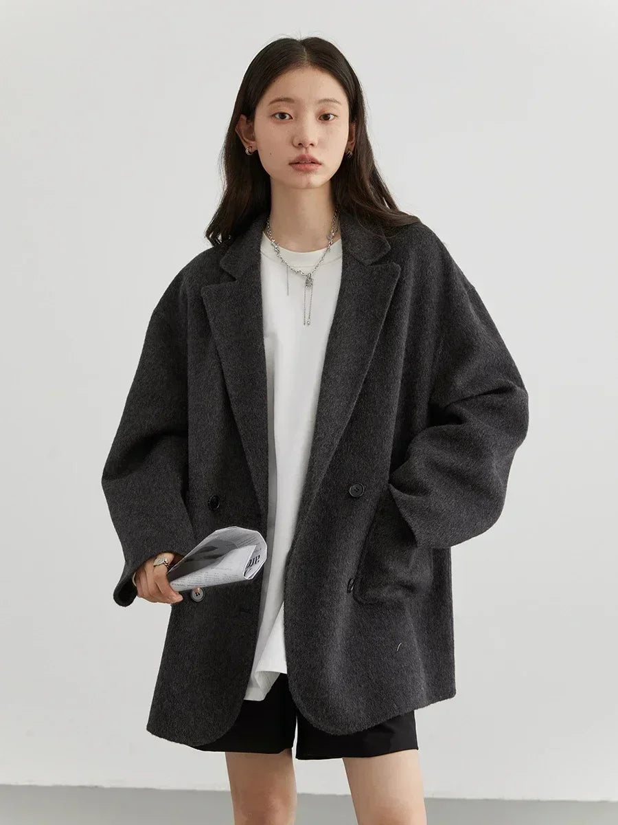Donna con giacca oversize grigia, maglietta bianca e pantaloncini neri. Moda casual autunnale, stile minimalista. Accessori: collana e borsa.