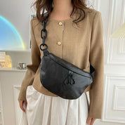 Donna con giacca beige e marsupio nero in pelle, catena decorativa. Moda femminile elegante, accessori trendy, abbigliamento casual chic.
