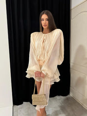 Donna con abito elegante color crema, maniche ampie, e borsa intrecciata beige. Moda femminile, abbigliamento chic, tendenze 2023.