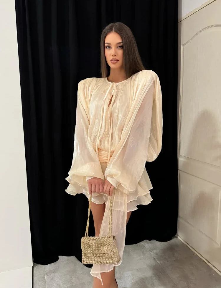 Donna con abito elegante color crema, maniche ampie, e borsa intrecciata beige. Moda femminile, abbigliamento chic, tendenze 2023.