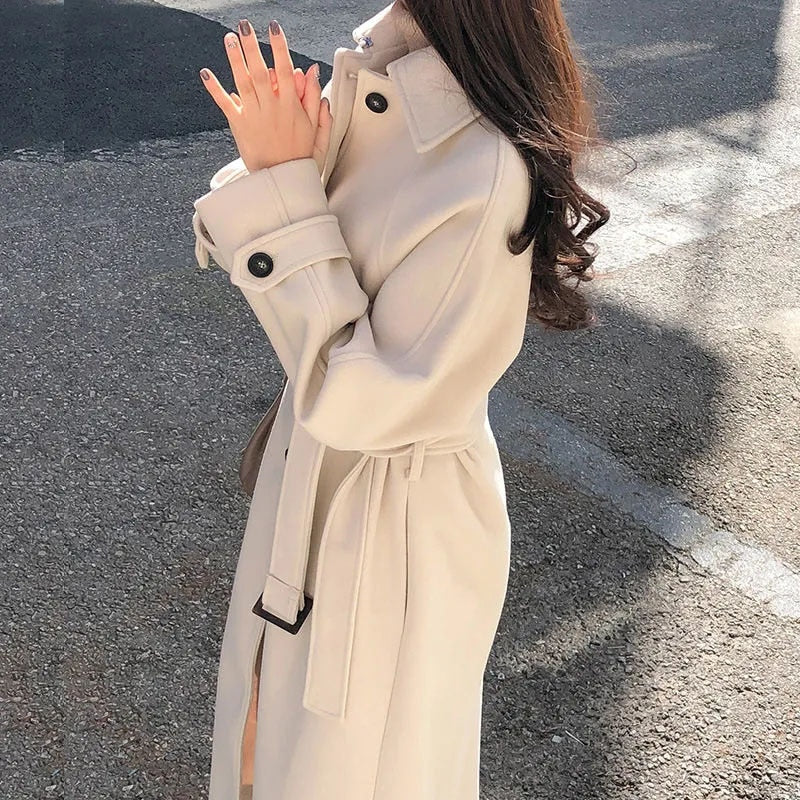 Cappotto beige elegante da donna, lungo con cintura, bottoni neri, indossato all'aperto. Moda autunnale, stile casual chic.