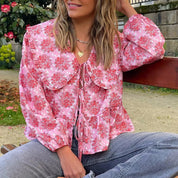 Blusa donna floreale rosa con maniche lunghe, colletto ampio e laccetti, indossata all'aperto. Moda casual primavera, abbigliamento femminile trendy.