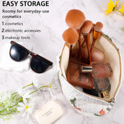 Astuccio cosmetico aperto su sfondo marmo, contiene pennelli trucco, profumo, occhiali da sole e accessori. Ideale per organizzare cosmetici quotidiani.