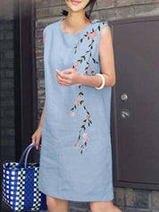 Abito estivo donna in lino blu con ricamo floreale rosa, senza maniche. Accessoriato con borsa a quadri blu e verde. Look casual elegante.