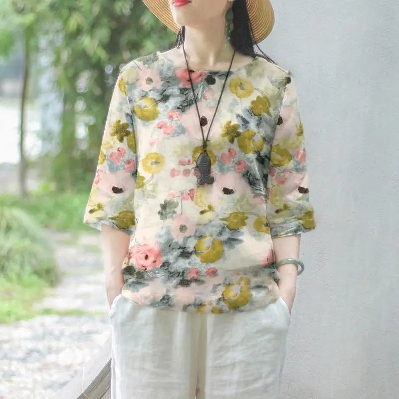 Maglietta floreale donna, maniche a tre quarti, colori pastello, stile casual estivo, indossata con pantaloni bianchi, sfondo naturale.