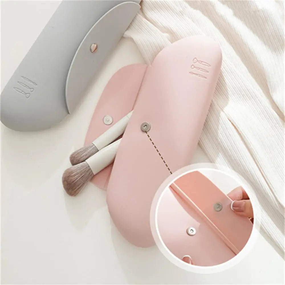 Custodia portapennelli trucco in silicone rosa e grigia, con chiusura a bottone. Include due pennelli per il trucco. Design elegante e pratico.