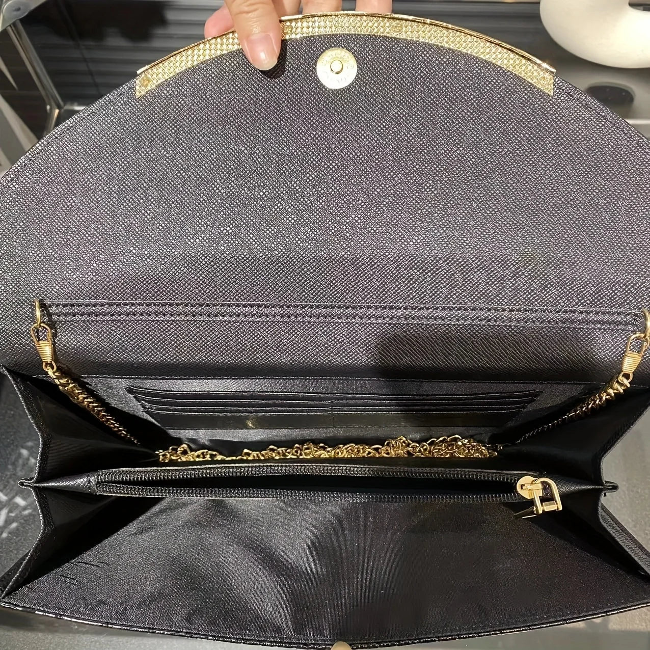 Elegante borsa a tracolla nera aperta, con catena dorata e chiusura magnetica. Design interno con scomparti multipli e dettagli raffinati.