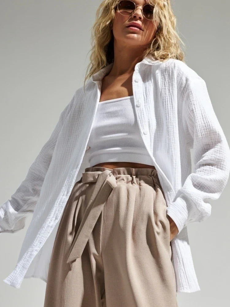 Donna con camicia bianca in cotone, top bianco e pantaloni beige a vita alta. Moda estiva, occhiali da sole, stile casual chic.