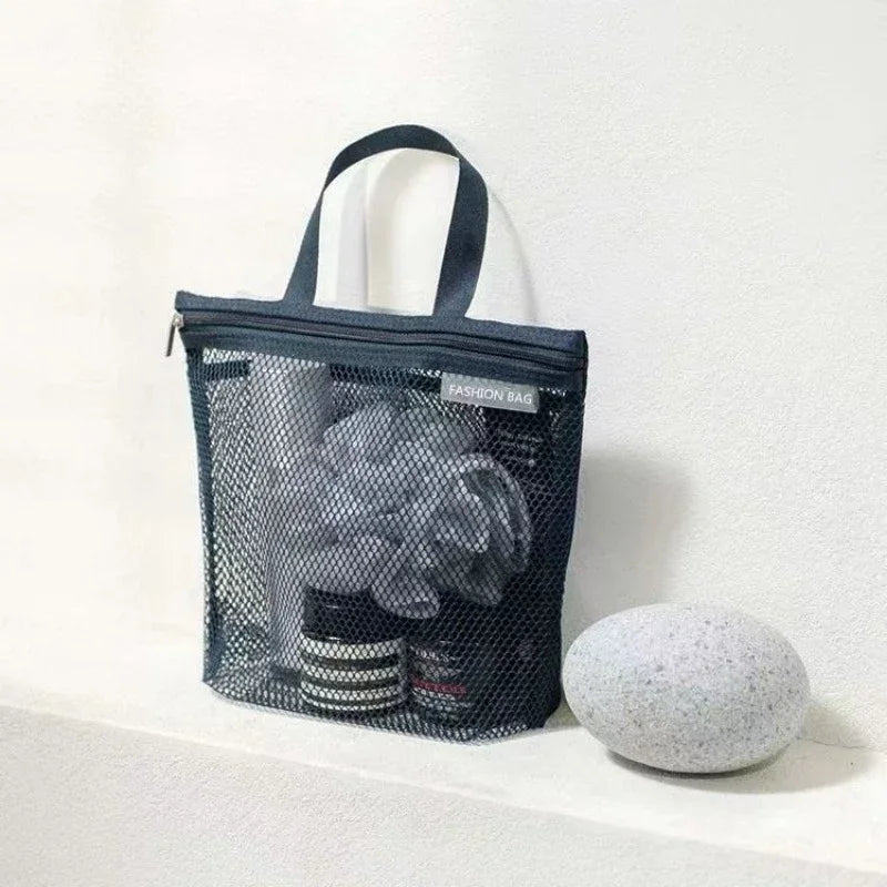 Borsa da toilette in rete nera con manico, contenente prodotti per la cura personale, su sfondo bianco. Accessorio da viaggio pratico ed elegante.
