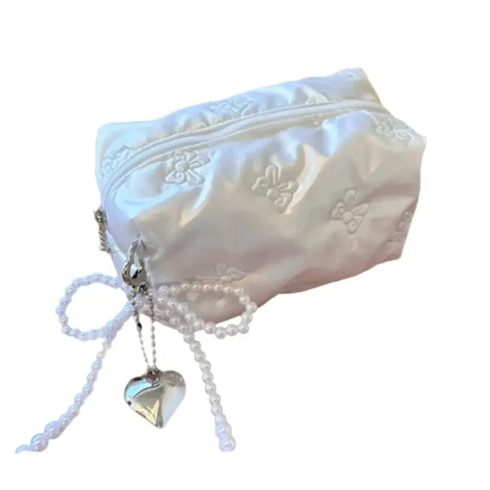 Elegante pochette bianca in raso con ricami floreali, chiusura a zip, decorata con fiocco di perle e ciondolo a cuore argentato. Perfetta per matrimoni.