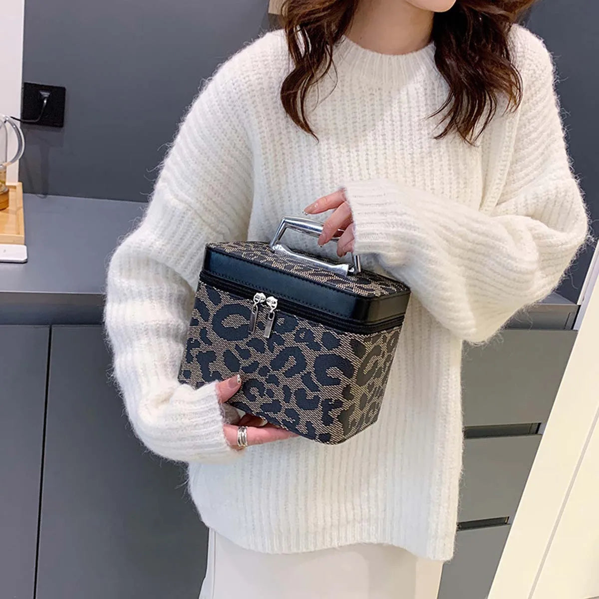 Donna con maglione bianco tiene borsa trucco leopardata con manico. Design elegante, ideale per cosmetici. Accessorio moda femminile.