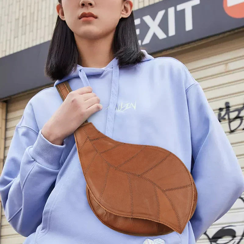 Giovane con felpa viola indossa borsa a tracolla marrone a forma di foglia. Moda urbana, accessori unisex, stile casual.