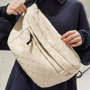 Borsa a tracolla beige intrecciata, indossata da una persona con maglia blu scuro. Design elegante e moderno, ideale per moda urbana e casual.