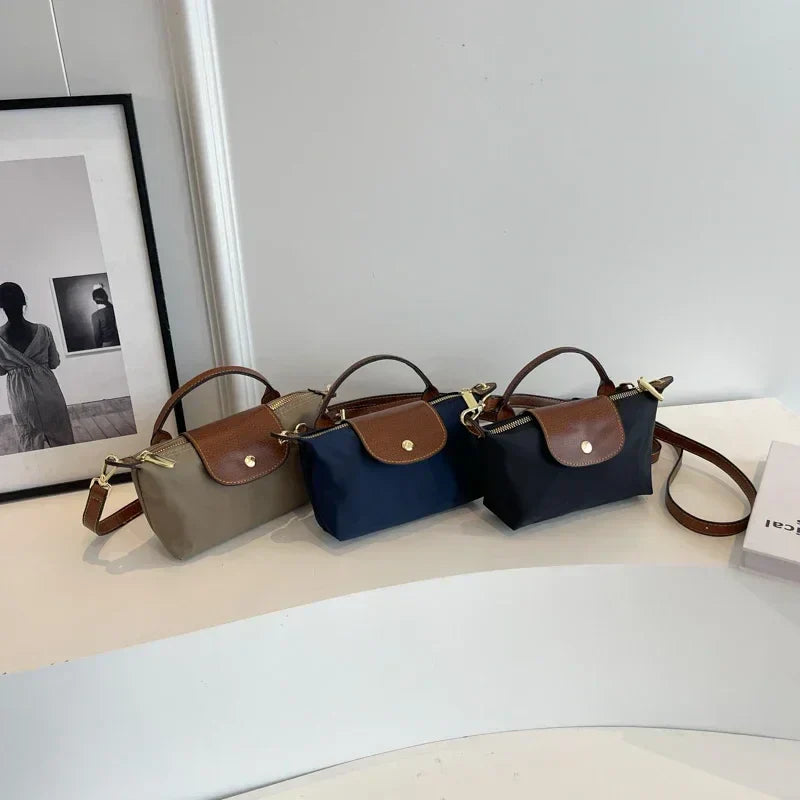 Tre borse a tracolla eleganti in tessuto e pelle, colori beige, blu e nero, su tavolo bianco. Design moderno, accessori moda donna.