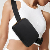 Donna con top bianco indossa marsupio nero a tracolla. Accessorio moda casual, ideale per viaggi e attività all'aperto. Design elegante e pratico.