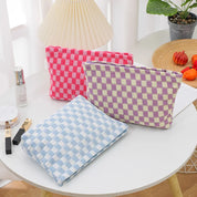 Tre pochette a quadri in tessuto, colori rosa, viola e azzurro, su tavolo bianco. Accessori moda, organizer da viaggio, design moderno.