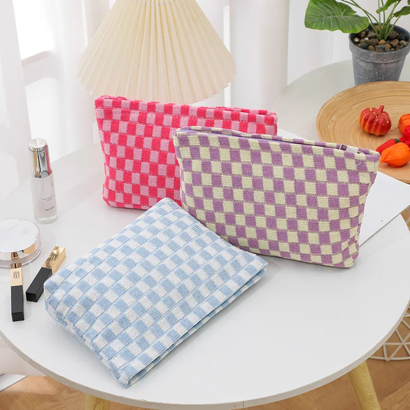 Tre pochette a quadri in tessuto, colori rosa, viola e azzurro, su tavolo bianco. Accessori moda, organizer da viaggio, design moderno.
