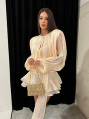 Donna con abito elegante color crema e borsa intrecciata, posa su sfondo nero. Moda femminile, abbigliamento da sera, stile sofisticato.