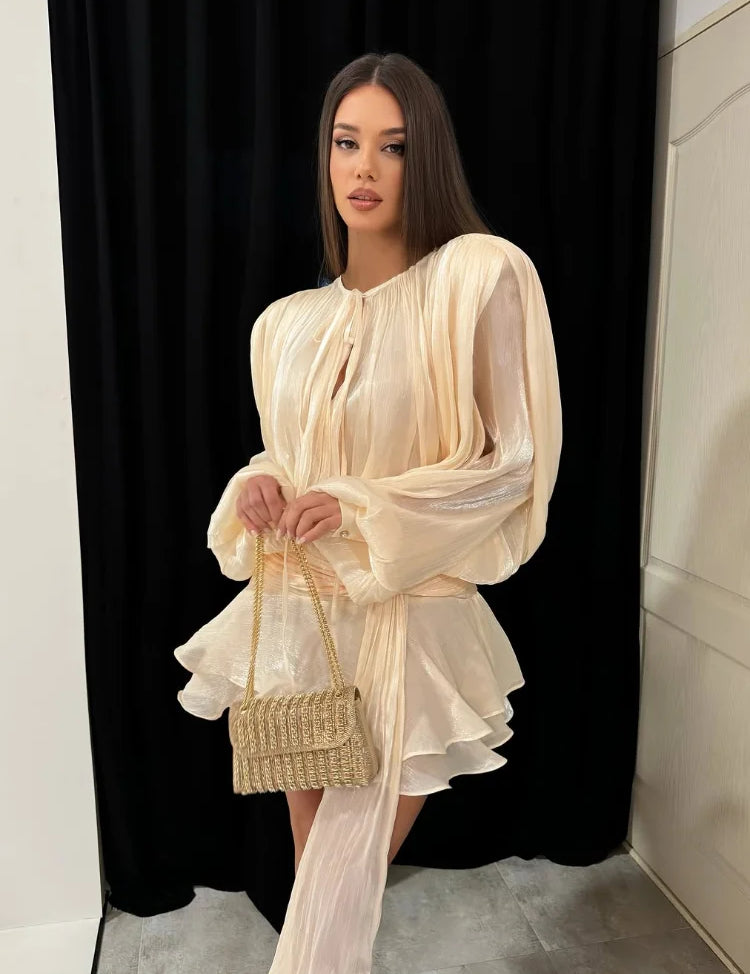 Donna con abito elegante color crema e borsa intrecciata, posa su sfondo nero. Moda femminile, abbigliamento da sera, stile sofisticato.