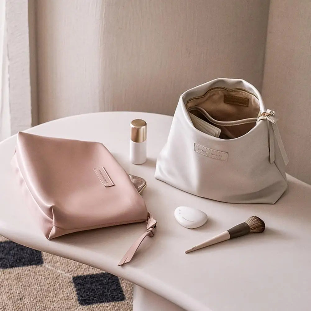 Due eleganti pochette in pelle su tavolo bianco, una rosa e una bianca, con accessori trucco. Design minimalista, ideale per cosmetici.