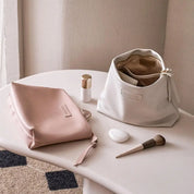 Due eleganti pochette in pelle su tavolo bianco, una rosa e una bianca, con accessori trucco. Design minimalista, ideale per cosmetici.