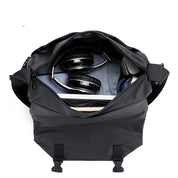 Borsa a tracolla nera aperta con cuffie, laptop e accessori all'interno. Design moderno, ideale per lavoro e viaggio. Accessori tecnologici inclusi.