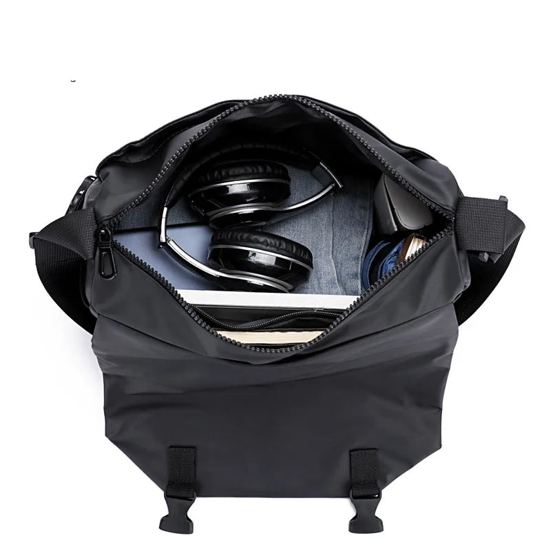 Borsa a tracolla nera aperta con cuffie, laptop e accessori all'interno. Design moderno, ideale per lavoro e viaggio. Accessori tecnologici inclusi.