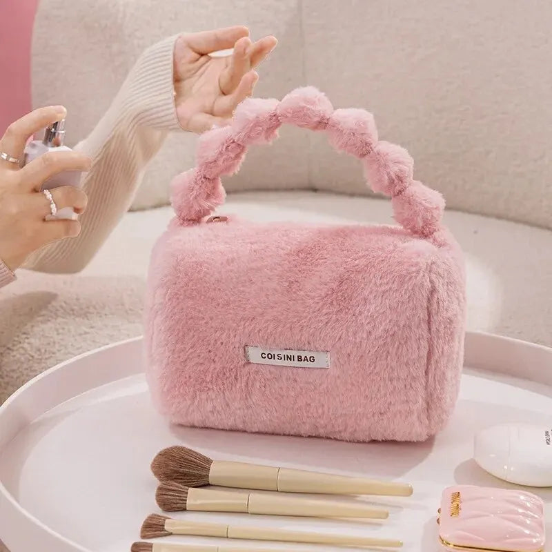 Borsa rosa in pelliccia sintetica con manico intrecciato, circondata da pennelli da trucco su un tavolo. Design elegante e moderno.
