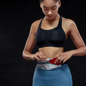 Donna in abbigliamento sportivo nero e blu inserisce uno smartphone in una cintura da corsa grigia. Accessorio fitness, corsa, sport.