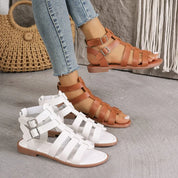 Sandali gladiatore in pelle marrone e bianca, con fibbie, indossati con jeans. Scarpe estive alla moda per donna, stile casual e comodo.