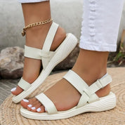 Sandali bianchi da donna con cinturino alla caviglia, suola ondulata, indossati con jeans bianchi. Scarpe estive eleganti e comode.