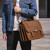 Uomo con giacca di jeans che indossa una borsa a tracolla in pelle marrone, stile vintage, all'aperto. Borsa elegante e funzionale per lavoro.