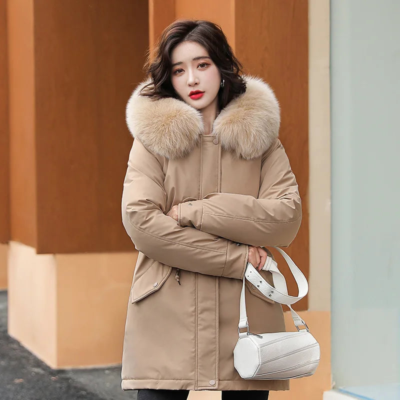 Giacca invernale donna beige con cappuccio in pelliccia sintetica, tasche laterali, abbinata a borsa bianca. Moda autunno-inverno 2023.