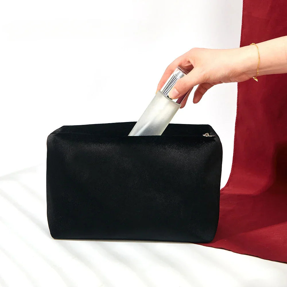 Mano inserisce flacone spray in borsa cosmetica nera su sfondo bianco e rosso. Accessori da viaggio, organizzazione trucco, beauty case elegante.
