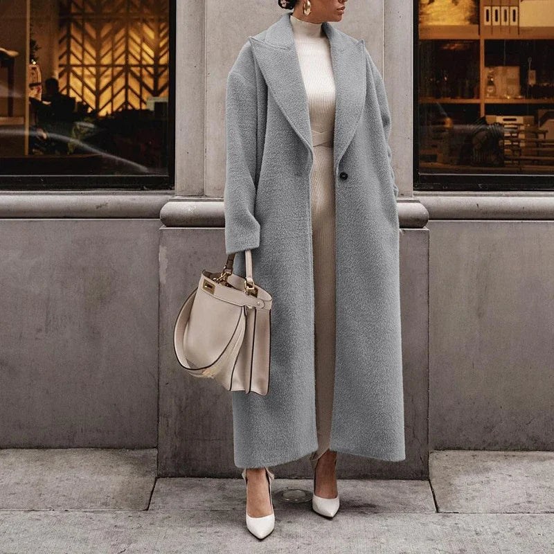 Cappotto lungo grigio donna elegante, abbinato a borsa beige e abito bianco. Moda autunnale, stile sofisticato, abbigliamento femminile chic.
