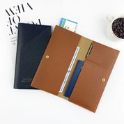 Portadocumenti in pelle marrone e nero su scrivania bianca, con tazza di caffè e rivista. Elegante organizer per ufficio, ideale per viaggi d'affari.