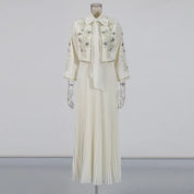 Abito lungo bianco elegante con ricami floreali, maniche lunghe e colletto a fiocco. Design plissettato, ideale per cerimonie e occasioni speciali.