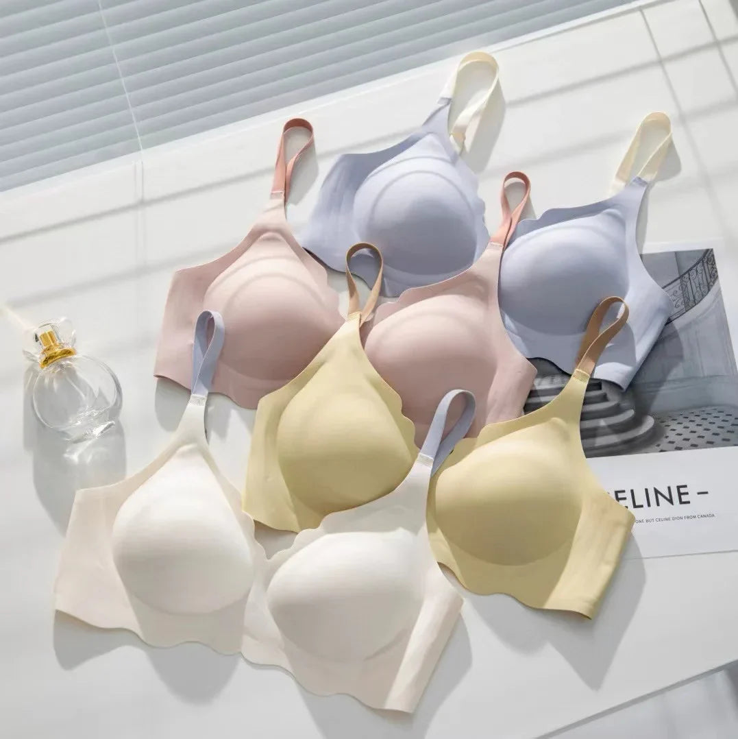 Reggiseni senza cuciture in vari colori pastello su sfondo bianco, con bottiglia di profumo. Intimo comodo e alla moda per donna.