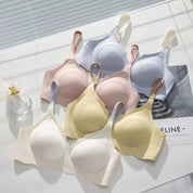 Reggiseni senza cuciture in vari colori pastello su sfondo bianco, con bottiglia di profumo. Intimo comodo e alla moda per donna.