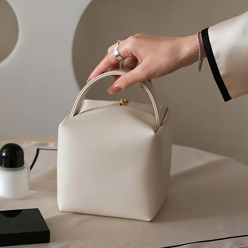 Borsa a mano in pelle bianca, design minimalista, chiusura dorata, su tavolo elegante. Accessorio moda donna, stile contemporaneo.