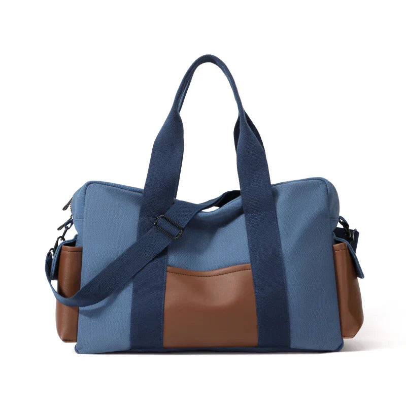 Borsa da viaggio in tela blu con dettagli in pelle marrone, manici robusti e tracolla regolabile. Design elegante e funzionale per viaggi.