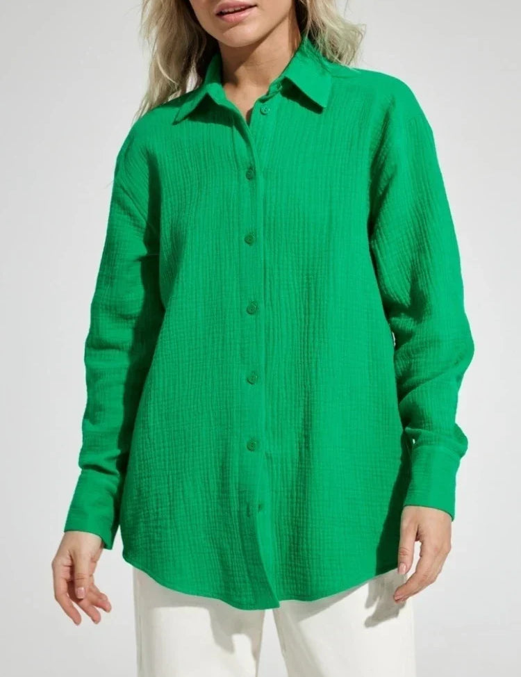 Camicia verde a maniche lunghe in tessuto leggero, con colletto classico e bottoni frontali, indossata da una donna. Moda casual elegante.