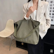 Donna con borsa a tracolla verde oliva, giacca a righe bianche, sedia moderna, interni minimalisti. Accessori moda donna eleganti e casual.