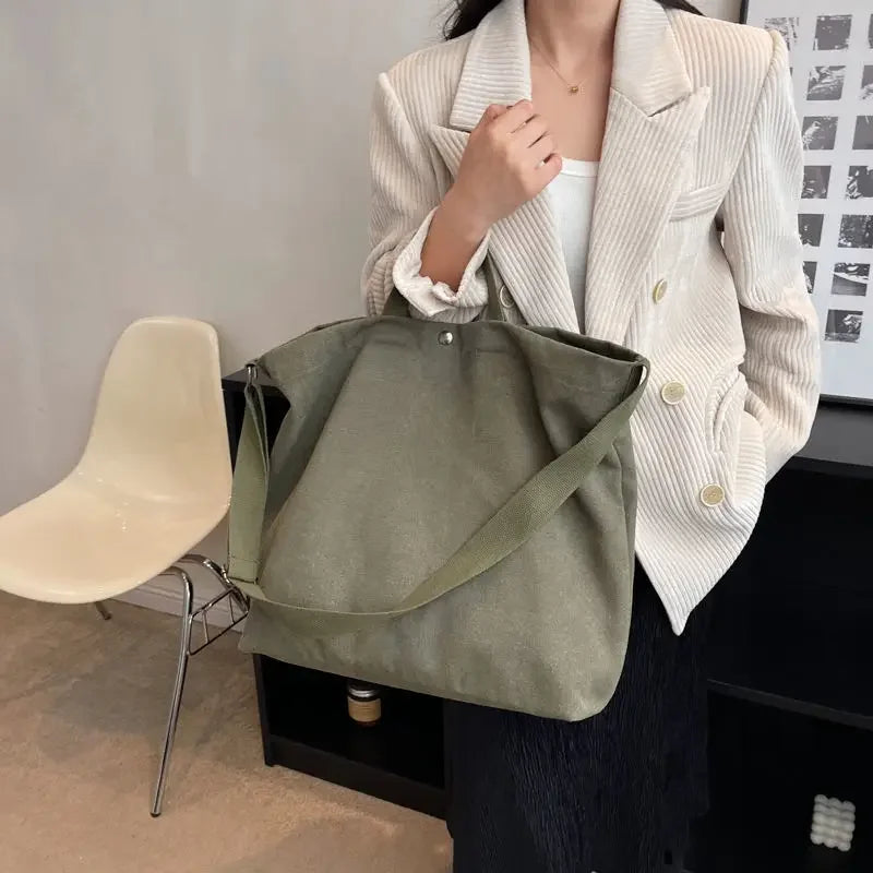 Donna con borsa a tracolla verde oliva, giacca a righe bianche, sedia moderna, interni minimalisti. Accessori moda donna eleganti e casual.