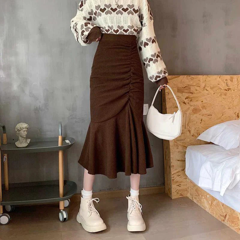 Gonna marrone a vita alta con arricciatura, abbinata a maglione bianco e marrone, borsa bianca e stivaletti beige. Moda autunnale elegante.