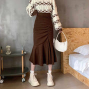 Gonna marrone a vita alta con arricciatura, abbinata a maglione bianco e marrone, borsa bianca e stivaletti beige. Moda autunnale elegante.
